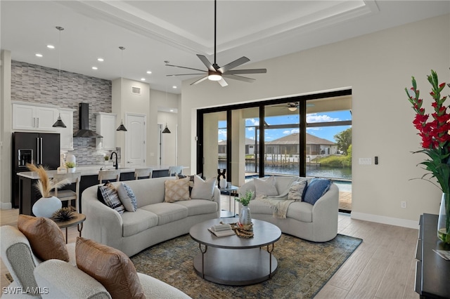 living room with ceiling fan, light hardwood / wood-style floors, a raised ceiling, and a water view