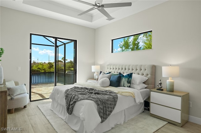 bedroom featuring access to outside, ceiling fan, light hardwood / wood-style flooring, and a tray ceiling