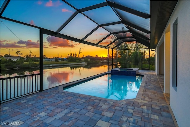 pool at dusk with an in ground hot tub, a patio, a water view, and glass enclosure