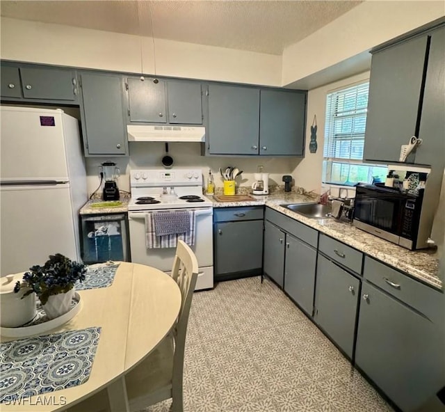 kitchen with white appliances, light countertops, a textured ceiling, under cabinet range hood, and a sink