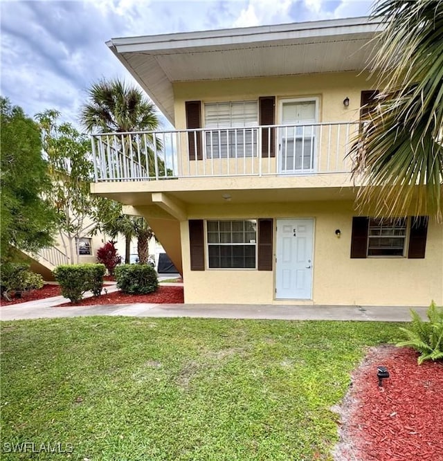 rear view of house with a yard, a balcony, and stucco siding