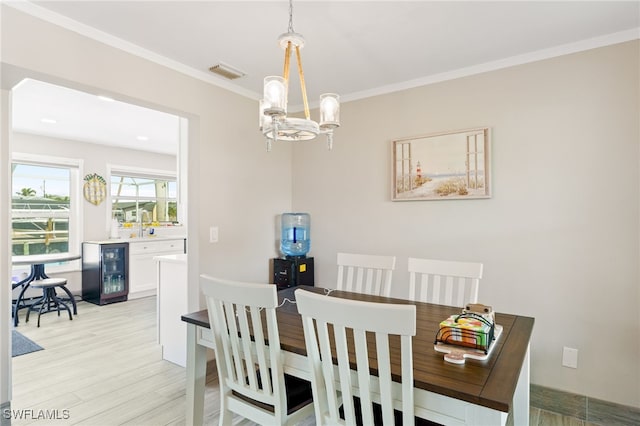 dining room with a notable chandelier, light hardwood / wood-style floors, ornamental molding, and beverage cooler