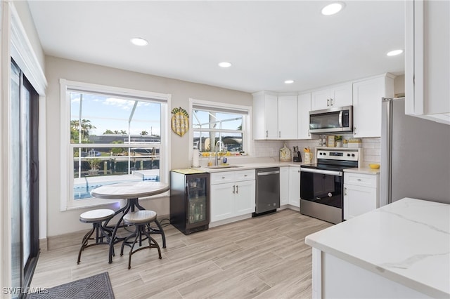 kitchen with white cabinetry, sink, beverage cooler, light stone counters, and appliances with stainless steel finishes