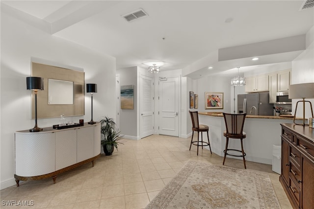 kitchen with white cabinetry, a chandelier, a kitchen bar, light tile patterned floors, and appliances with stainless steel finishes