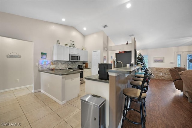 kitchen with kitchen peninsula, appliances with stainless steel finishes, a kitchen bar, vaulted ceiling, and white cabinetry