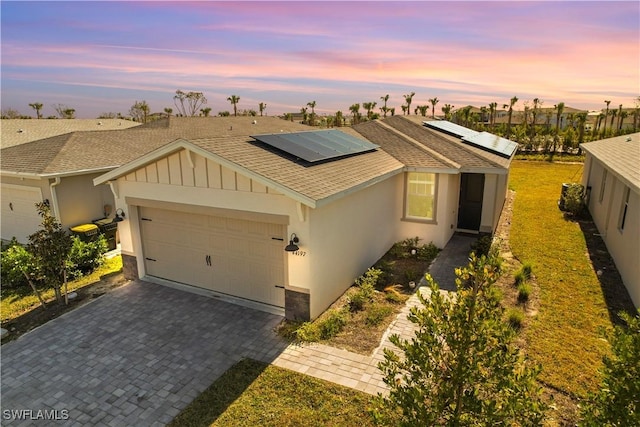 view of front of house with a garage, a shingled roof, solar panels, decorative driveway, and stucco siding