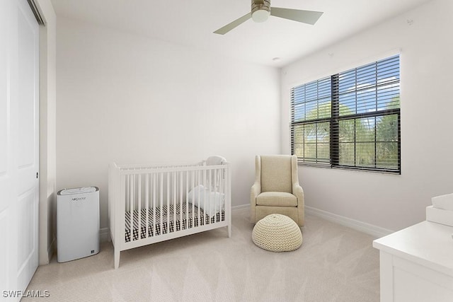 bedroom with ceiling fan, a closet, light colored carpet, and a nursery area