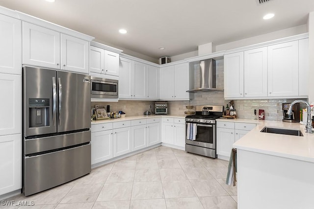 kitchen featuring sink, wall chimney exhaust hood, backsplash, white cabinets, and appliances with stainless steel finishes