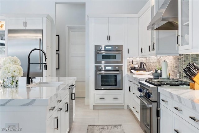 kitchen featuring white cabinets, wall chimney exhaust hood, premium appliances, and tasteful backsplash