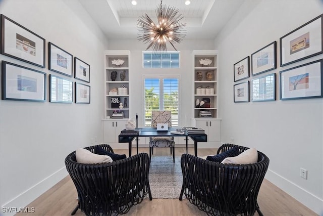 home office with a raised ceiling, built in features, light wood-type flooring, and an inviting chandelier