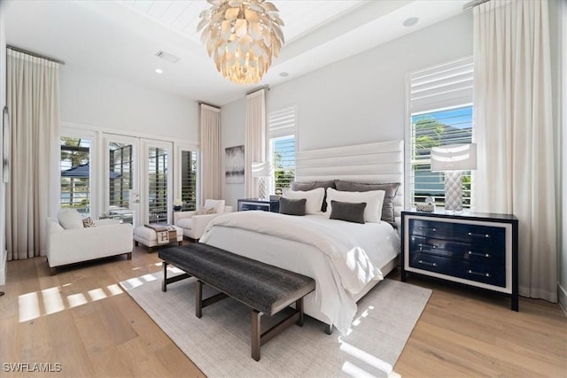 bedroom featuring a chandelier, french doors, light wood-type flooring, and a raised ceiling