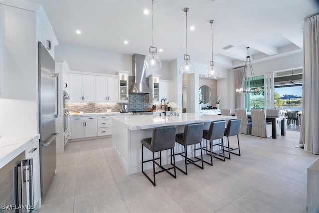 kitchen with pendant lighting, white cabinets, a spacious island, wall chimney range hood, and light stone counters