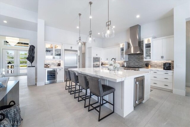 kitchen with appliances with stainless steel finishes, wine cooler, wall chimney range hood, white cabinetry, and a large island