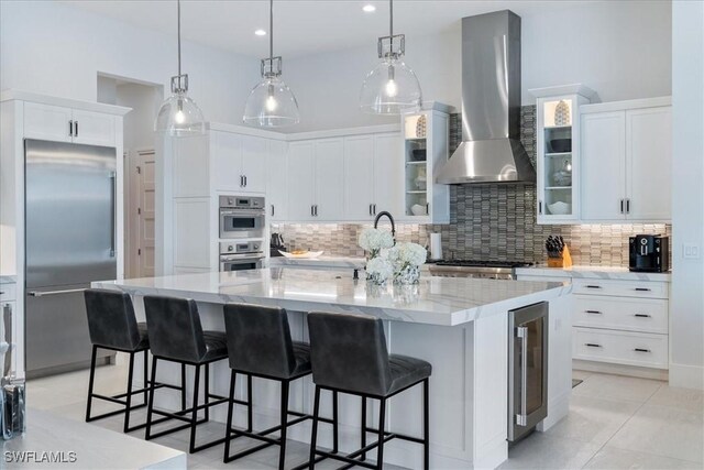 kitchen with decorative backsplash, appliances with stainless steel finishes, a spacious island, wall chimney range hood, and wine cooler