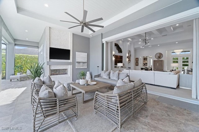 living room with ceiling fan with notable chandelier, beam ceiling, a large fireplace, and a wealth of natural light