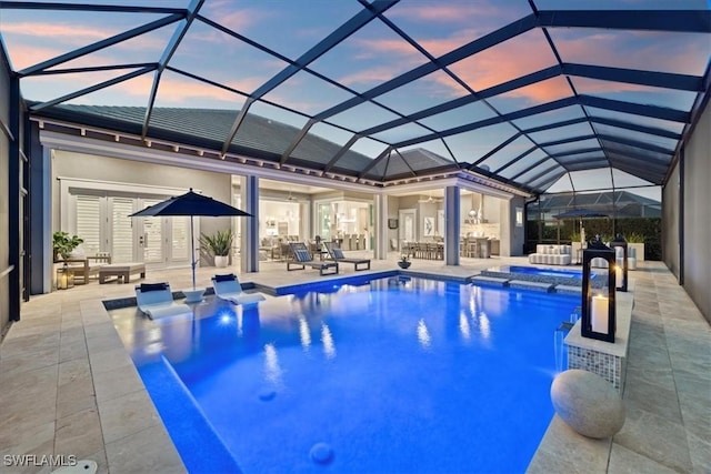 pool at dusk with an in ground hot tub, glass enclosure, and a patio area