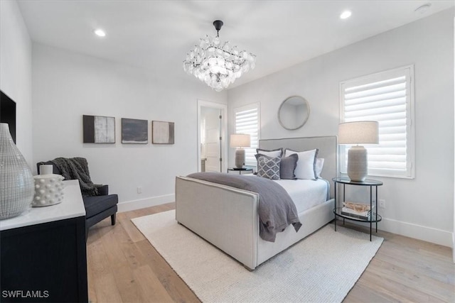 bedroom with light hardwood / wood-style flooring, ensuite bath, and a notable chandelier