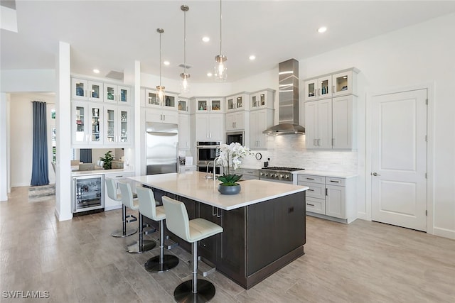 kitchen featuring beverage cooler, wall chimney range hood, built in appliances, a spacious island, and decorative light fixtures