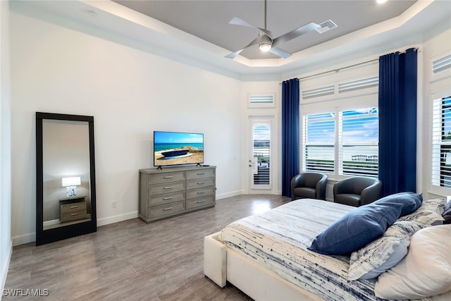 bedroom with access to outside, a tray ceiling, ceiling fan, and light hardwood / wood-style floors