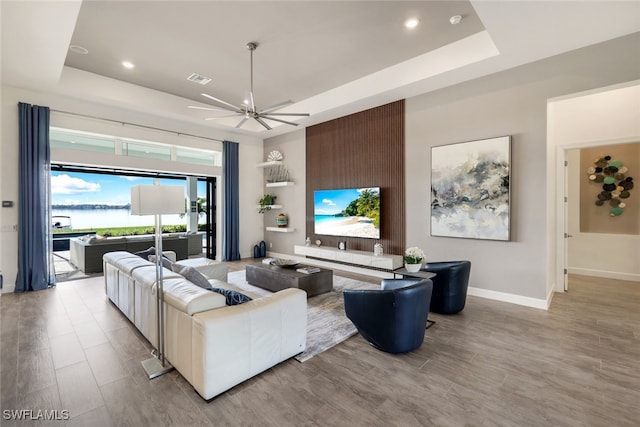 living room with light hardwood / wood-style floors, a raised ceiling, and ceiling fan