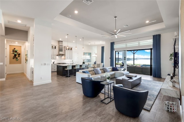 living room featuring hardwood / wood-style floors, a raised ceiling, and ceiling fan