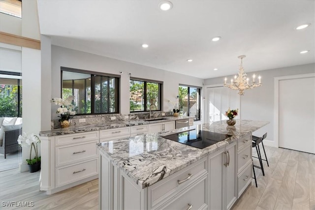 kitchen with a center island, black electric stovetop, sink, light stone counters, and white cabinetry