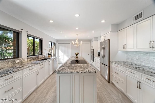 kitchen with light stone countertops, stainless steel appliances, sink, white cabinets, and a center island