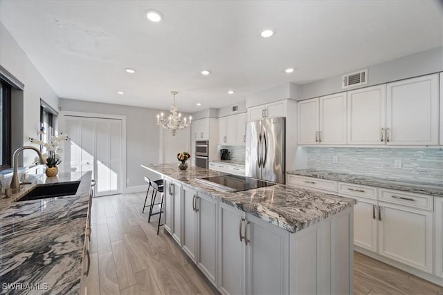 kitchen with appliances with stainless steel finishes, a spacious island, sink, decorative light fixtures, and white cabinetry