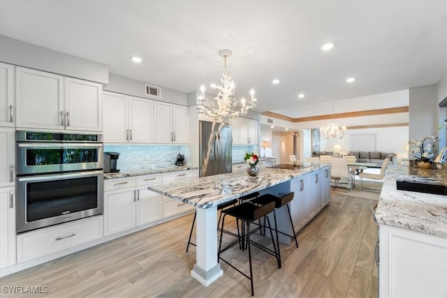 kitchen with white cabinetry, light stone countertops, a chandelier, a breakfast bar, and appliances with stainless steel finishes