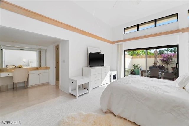 carpeted bedroom with access to exterior, built in desk, a towering ceiling, and ensuite bath