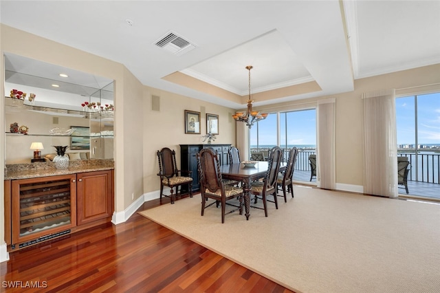 dining space with wine cooler, dark hardwood / wood-style flooring, a notable chandelier, a tray ceiling, and a water view