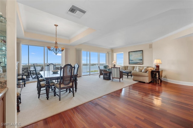 dining room featuring an inviting chandelier, a raised ceiling, a water view, crown molding, and hardwood / wood-style flooring