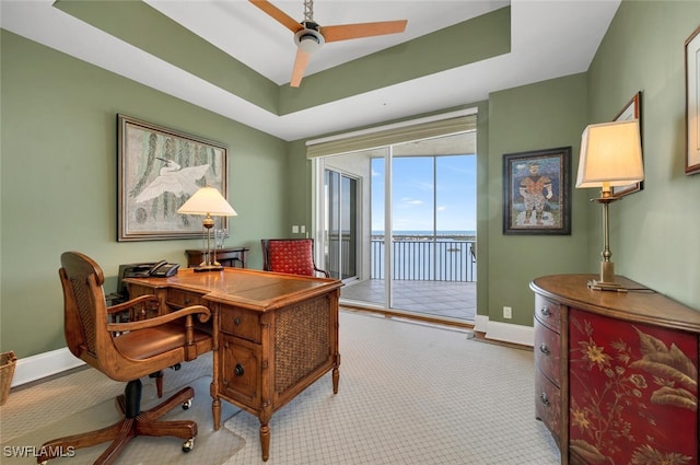 carpeted home office featuring a water view, a raised ceiling, and ceiling fan