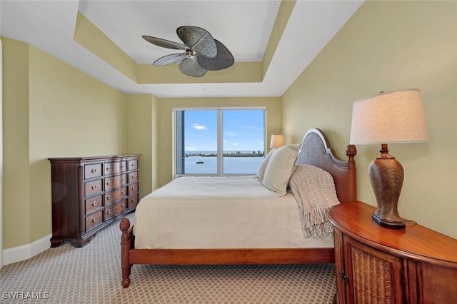 carpeted bedroom featuring a tray ceiling, ceiling fan, and a water view