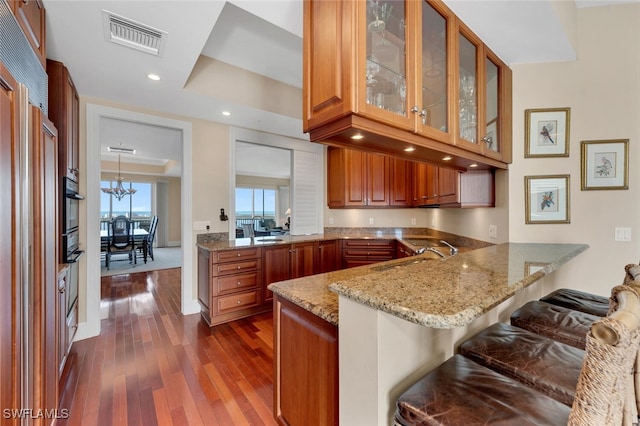 kitchen with kitchen peninsula, a kitchen bar, light stone countertops, sink, and pendant lighting