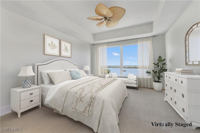 bedroom featuring light colored carpet, a tray ceiling, a water view, and ceiling fan