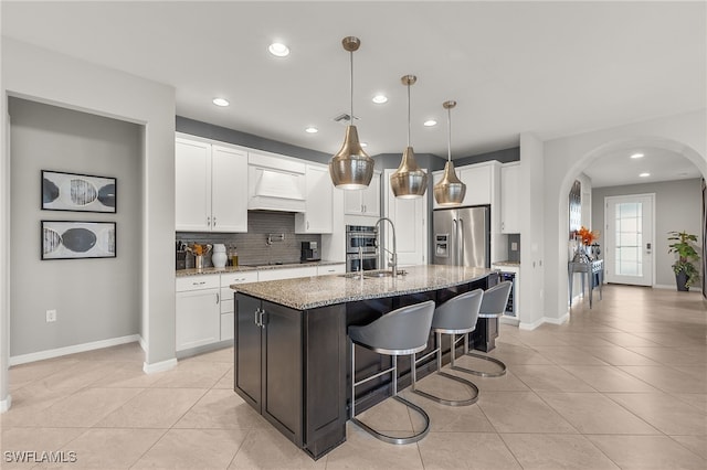 kitchen featuring light stone countertops, appliances with stainless steel finishes, pendant lighting, a center island with sink, and white cabinets