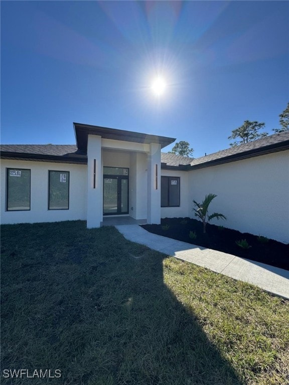 rear view of house featuring a yard and stucco siding