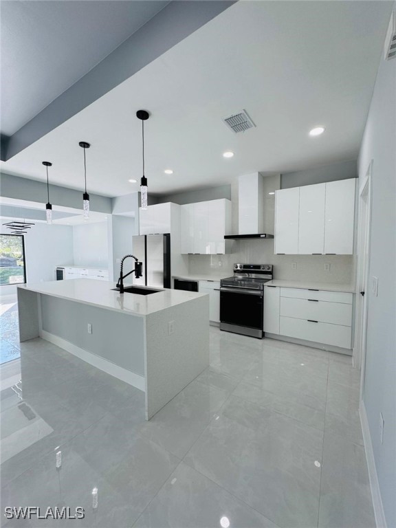 kitchen with white cabinetry, wall chimney range hood, an island with sink, pendant lighting, and appliances with stainless steel finishes