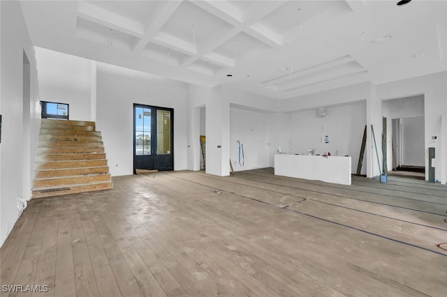 unfurnished living room with a towering ceiling, beamed ceiling, coffered ceiling, and light hardwood / wood-style flooring