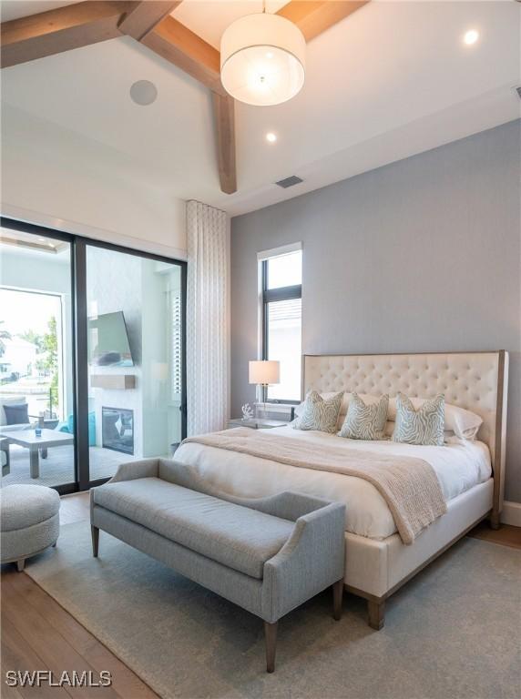 bedroom featuring beam ceiling, access to exterior, hardwood / wood-style floors, and multiple windows