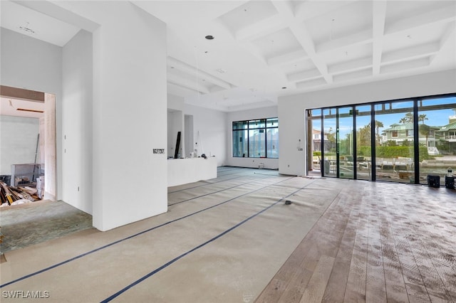 unfurnished living room featuring beam ceiling, coffered ceiling, light hardwood / wood-style floors, and a high ceiling