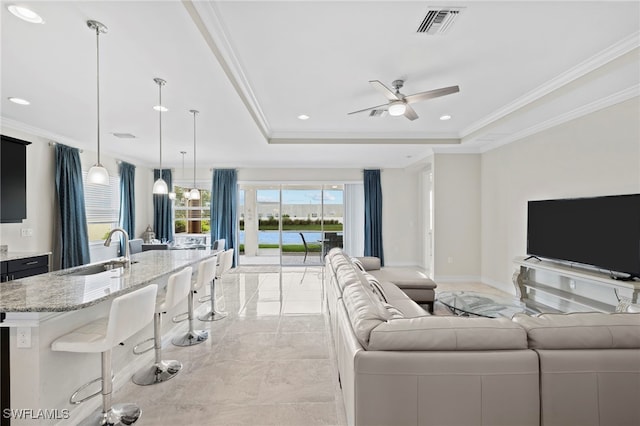 living room featuring ceiling fan, crown molding, sink, and a tray ceiling