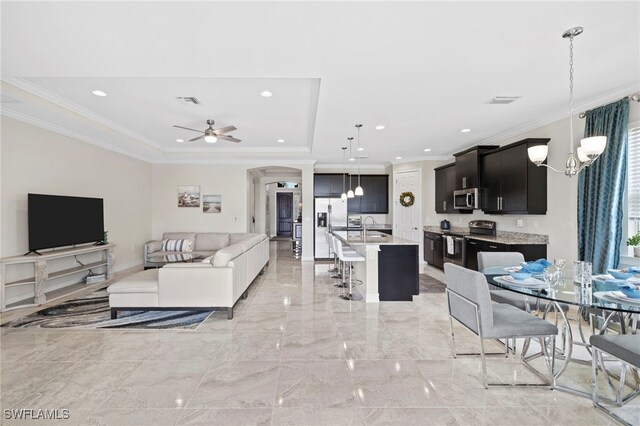 living room featuring a raised ceiling, crown molding, sink, and ceiling fan with notable chandelier