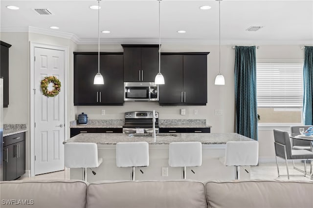 kitchen with sink, hanging light fixtures, stainless steel appliances, a kitchen bar, and a kitchen island with sink