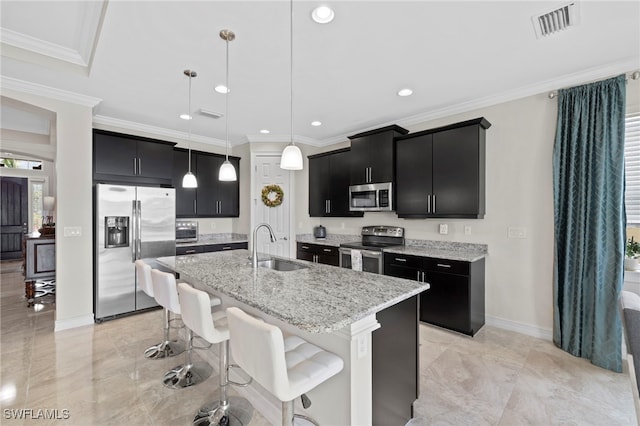 kitchen featuring light stone countertops, appliances with stainless steel finishes, sink, decorative light fixtures, and a center island with sink