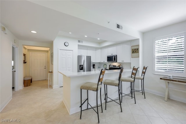 kitchen with a kitchen breakfast bar, white cabinetry, kitchen peninsula, and appliances with stainless steel finishes