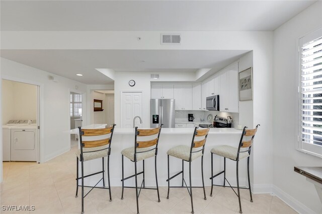 kitchen featuring washer and clothes dryer, a breakfast bar, sink, white cabinetry, and stainless steel appliances