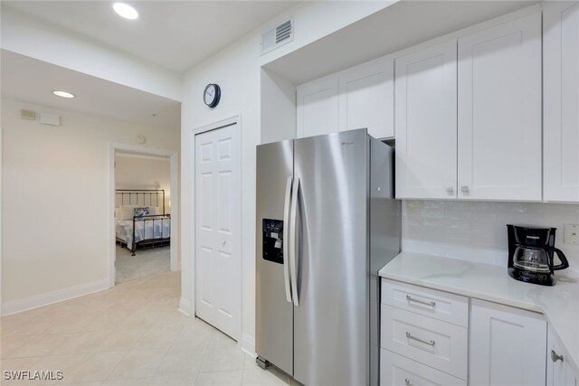 kitchen featuring backsplash, light tile patterned floors, white cabinets, and stainless steel refrigerator with ice dispenser