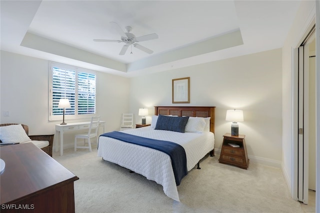 carpeted bedroom with ceiling fan and a tray ceiling